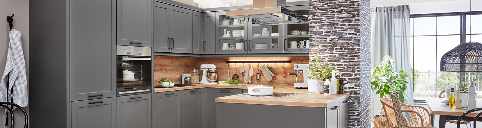 Contemporary kitchen with gray cabinets, wooden counters, steel appliances, and ample natural light from garden-facing windows.