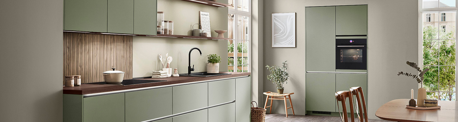 Modern kitchen interior with clean white cabinetry, high-end appliances, and a relaxed woman enjoying a beverage in a cozy, stylish chair.